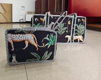 Puede incluir: Dos bolsos rectangulares acolchados con fondo negro y un patrón repetitivo de leopardos amarillos y blancos, hojas de palmera verdes y aves tropicales. Los bolsos tienen bordes y asas de tela con rayas blancas y negras.