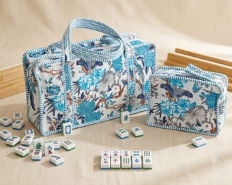 Puede incluir: Un bolso de tela acolchada y un estuche rectangular más pequeño a juego, ambos con un estampado floral y de aves en azul sobre fondo blanco y ribetes a rayas azules. Alrededor hay fichas de mahjong blancas con caracteres azules y verdes.
