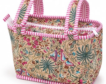 May include: A rectangular quilted fabric bag featuring a beige base with a colorful floral and butterfly print in shades of pink, teal, and brown. The bag has two handles and a top zipper closure, all accented with pink and white striped trim.
