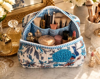 May include: A quilted makeup bag featuring a blue and white floral pattern on the exterior and a blue and white striped interior lining. The bag is open and filled with various cosmetic items, including makeup brushes, tubes, and compacts.