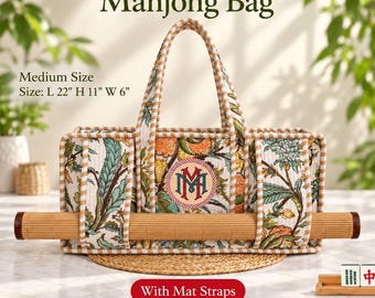 May include: A rectangular fabric Mahjong bag with a beige and white striped trim, featuring a floral pattern in green and orange. It includes a central monogram, two handles, and integrated straps holding a rolled bamboo mat. Size: L 22" H 11" W 6".