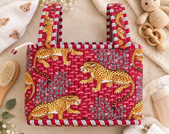May include: A quilted fabric storage basket featuring a red background with a repeating pattern of yellow leopards and green foliage. The basket has two upright handles with a red and white striped trim along the edges and seams.