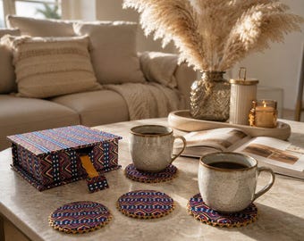 May include: A rectangular storage box with a hinged lid and a yellow pull tab, featuring a dark blue fabric with a geometric pattern of red, white, and yellow zigzags. Three matching circular coasters are placed on the table surface.