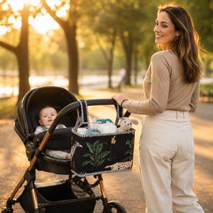May include: A black stroller organizer bag featuring a jungle-themed print with green palm leaves, a zebra, and a leopard. The rectangular bag has black and white striped trim, two top handles, and is attached to the handlebar of a black baby stroller.