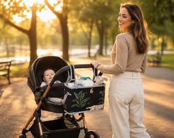 May include: A black stroller organizer bag featuring a jungle-themed print with green palm leaves, a zebra, and a leopard. The rectangular bag has black and white striped trim, two top handles, and is attached to the handlebar of a black baby stroller.