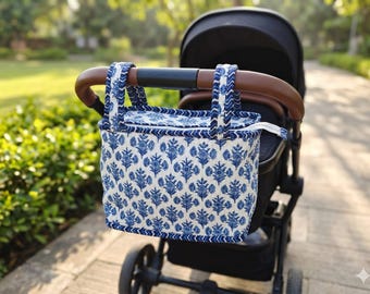 May include: A rectangular fabric stroller organizer bag featuring a blue and white floral block print pattern. The bag has a zippered top closure and two matching fabric straps with a chevron trim, hanging from the brown handlebar of a black stroller.