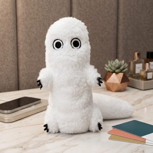 May include: A white plush toy with a soft, furry texture, featuring two large, circular black eyes and small black claws on its hands and feet. The creature has an upright, cylindrical body with a long, thick tail extending to the right side.