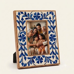 May include: A rectangular picture frame with a light brown wooden border and an inlaid white surface featuring a blue floral and vine pattern. The frame holds a photograph of a family of five, including two adults, two children, and one elder.
