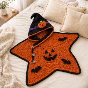 May include: A star-shaped crochet blanket with a hood, featuring a vibrant orange base with a black spiderweb pattern, three black bat appliques, and a central jack-o'-lantern face. The hood is black with a purple band and a small pumpkin applique.