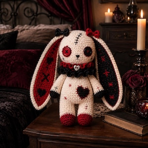 May include: A cream-colored crochet rabbit doll with long ears, one red and one black. It features button eyes, a stitched forehead, a black and red ruffled collar with a heart charm, and a black heart patch on its chest with red accents.
