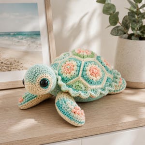 May include: A crocheted turtle toy featuring a shell constructed from hexagonal motifs in shades of mint green, cream, and soft pink. The head and flippers are crafted in a matching cream and mint green yarn, with large, round, black plastic eyes.