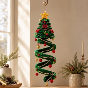 Op de afbeelding: Een hangend spiraalvormig kerstboomornament gehaakt van donkergroen garen. De boom is bekroond met een gele ster en versierd met kleine rode strikjes, rode bessen, gouden kralen en rode bollen die aan de groene spiraalstructuur hangen.