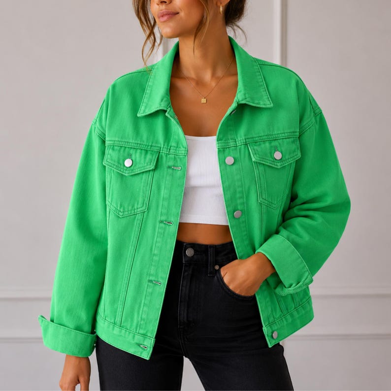 May include: A bright green denim jacket featuring a classic collar, long sleeves with buttoned cuffs, and two chest pockets with button-down flaps. The jacket has a front button closure and is worn over a white crop top and black jeans.