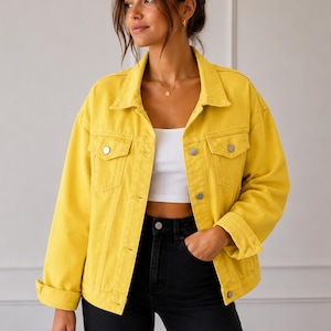 May include: A bright yellow denim jacket featuring a classic collar, long sleeves with folded cuffs, and two chest pockets with silver-toned metal buttons. The jacket is worn open over a plain white crop top and black high-waisted denim pants.