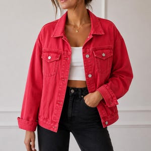 May include: A bright red denim jacket featuring a classic collar, long sleeves with buttoned cuffs, and two chest pockets with button-down flaps. The jacket is worn open over a plain white crop top, paired with black denim jeans with a button fly.