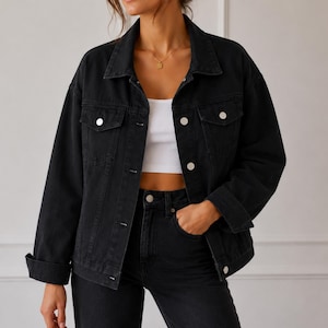 May include: A black denim jacket featuring a classic collar, long sleeves with buttoned cuffs, and two chest pockets with button-down flaps. The jacket is worn open over a white crop top, showcasing silver-toned metal buttons down the front placket.