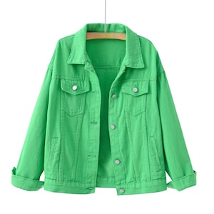 May include: A bright green denim jacket featuring a classic collar, long sleeves with buttoned cuffs, and a front button closure. The jacket includes two chest pockets with buttoned flaps and two vertical side pockets, all finished with silver buttons.