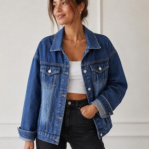 May include: A medium-wash blue denim jacket featuring a classic collar, long sleeves with folded cuffs, two chest pockets with button flaps, and a front button closure. The jacket has a relaxed fit with subtle distressed vertical detailing on the front.