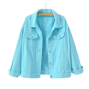 May include: A bright turquoise denim jacket featuring a classic collar, long sleeves with folded cuffs, two chest pockets with button flaps, and a front button closure. The jacket is constructed with visible seams and silver-toned metal buttons.