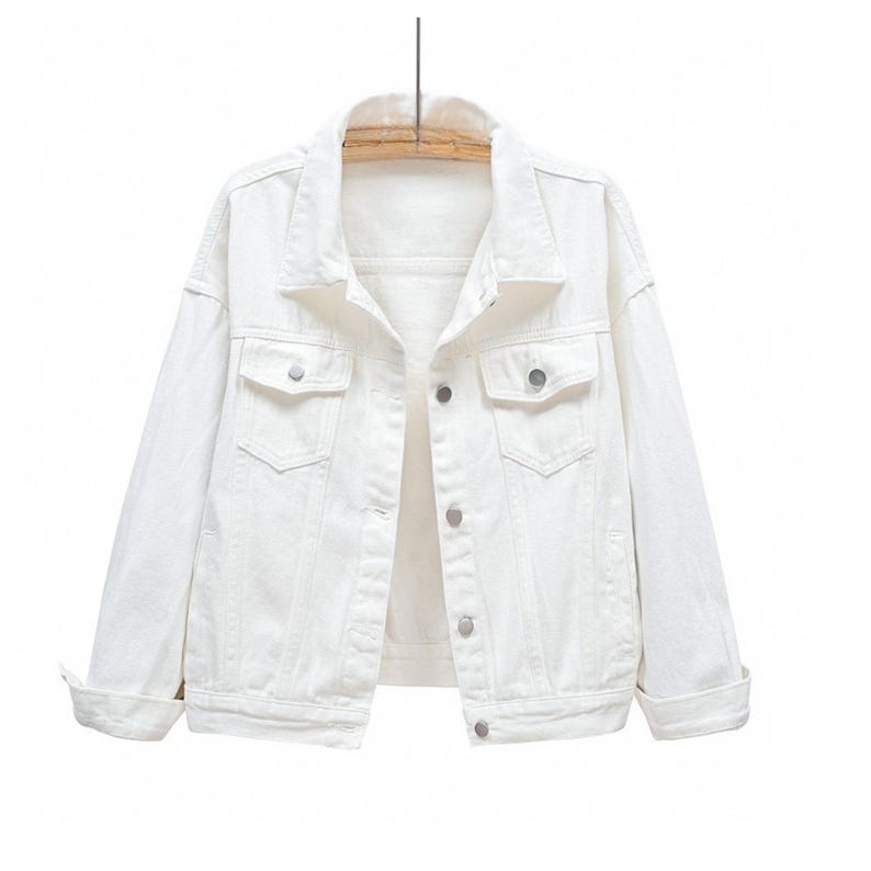 May include: A solid white denim jacket featuring a classic collar, long sleeves with folded cuffs, and a front button-down closure. The garment includes two chest pockets with buttoned flaps and a structured hemline, presented on a wooden hanger.