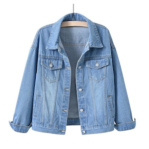 May include: A light blue denim jacket featuring a classic collar, long sleeves with folded cuffs, two chest pockets with button flaps, and a front button closure. The jacket has a light wash finish with subtle distressed detailing on the front.