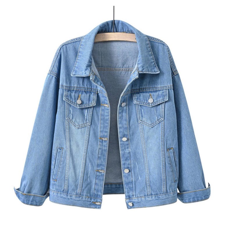 May include: A light blue denim jacket featuring a classic collar, long sleeves with folded cuffs, two chest pockets with button flaps, and a front button closure. The jacket has a light wash finish with subtle distressed detailing on the front.