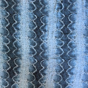 May include: A fabric featuring a repeating vertical pattern of light blue and dark charcoal grey scales. The design consists of alternating columns of textured, open-weave mesh and solid, snake-like scale shapes that create a layered visual effect.