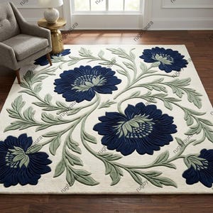 May include: A rectangular area rug featuring a cream-colored background with a large-scale floral pattern. The design includes deep navy blue blossoms and light sage green swirling leaves and stems, creating a continuous botanical motif.