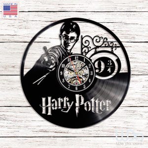 Puede incluir: Un reloj de pared circular hecho de un disco de vinilo negro con la silueta recortada de un personaje sosteniendo una varita, el texto Harry Potter y el número 9 3/4. El centro muestra una esfera con números negros y manecillas plateadas.