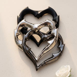 May include: Three heart-shaped carabiners with a spiked, thorny edge design. One carabiner is matte black, one is polished silver, and one is a dark gunmetal grey. Each features a spring-loaded gate mechanism for opening and closing the heart frame.