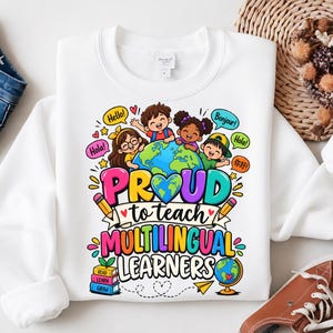 Op de afbeelding: Een wit sweatshirt met ronde hals en een kleurrijke afbeelding van vier kinderen rond een wereldbol. De tekst luidt PROUD to teach MULTILINGUAL LEARNERS, met tekstballonnen met Hello, Bonjour, Hola en Ni Hao.