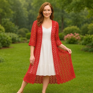 May include: A long, open-front red crochet cardigan featuring a delicate, repeating diamond-shaped lace pattern, three-quarter length sleeves, and a scalloped hemline, worn over a simple, sleeveless white knee-length dress with a tiered skirt.