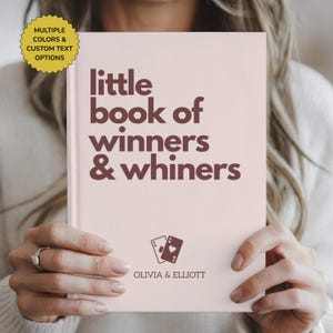May include: A light pink hardcover book with dark brown text that reads little book of winners & whiners. Below the text is a graphic of two playing cards and the names OLIVIA & ELLIOTT. A yellow starburst badge states multiple colors & custom text options.