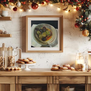 May include: A square framed oil painting depicting a glass bowl filled with green and black olives in a light-colored liquid. The artwork is displayed on a wall above a wooden kitchen counter featuring various baked goods and holiday decorations.