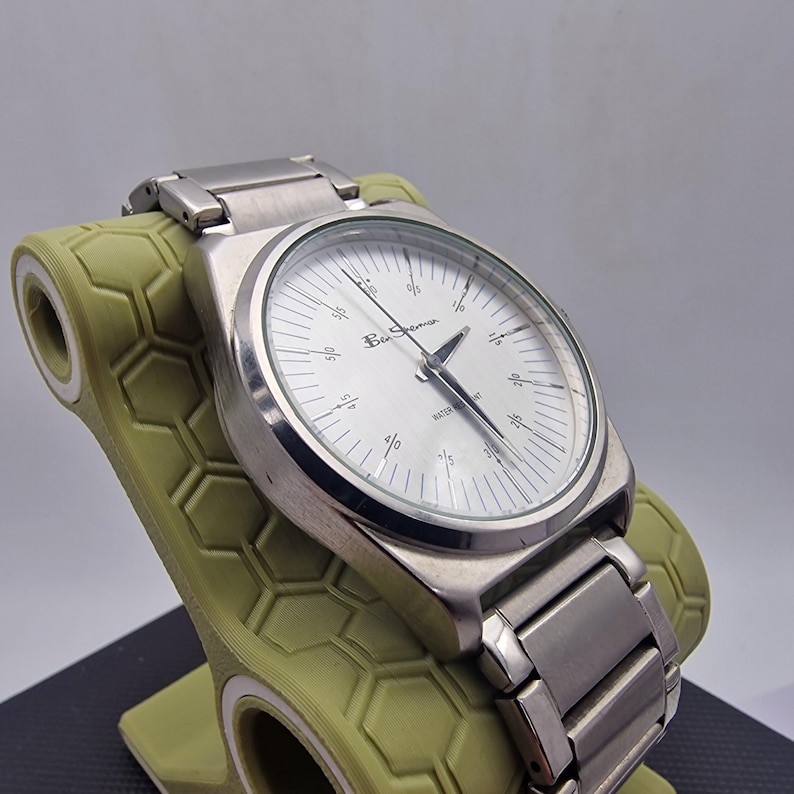 A authentic pre-owned Ben Sherman BS095 Men's Quartz Watch. Featuring a unique brushed silver analogue display, this timepiece stands out with its striking blue-accented numerical markers and precise 3-hand design. The durable stainless steel case is paired with a matching silver-toned metal link bracelet,