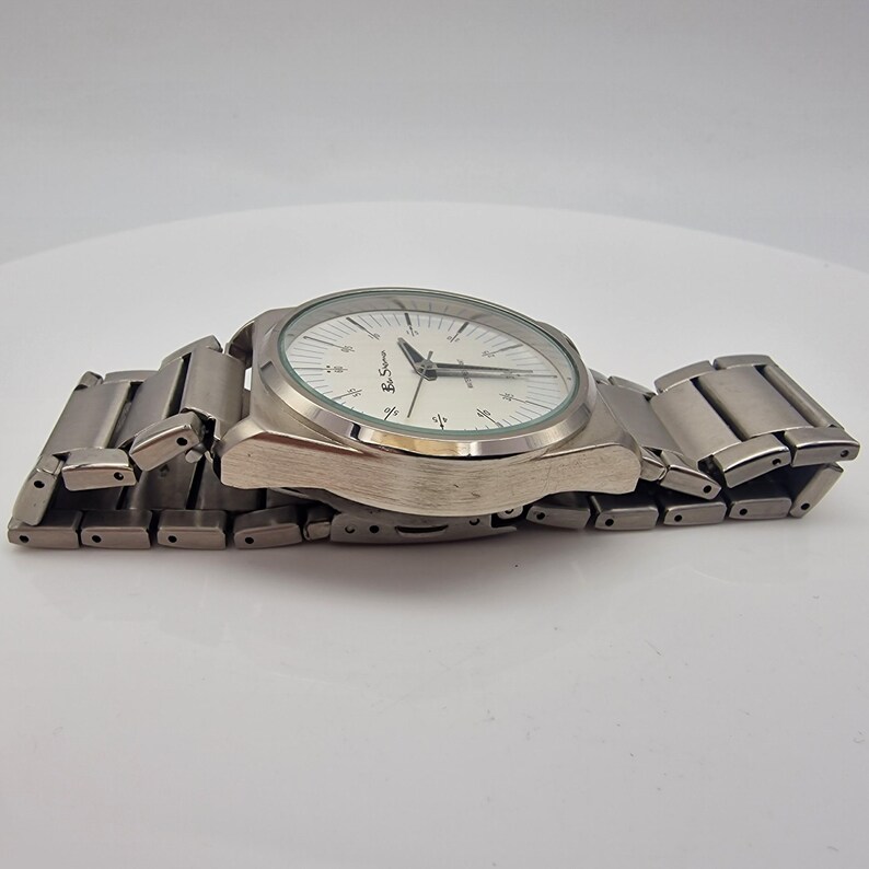 A authentic pre-owned Ben Sherman BS095 Men's Quartz Watch. Featuring a unique brushed silver analogue display, this timepiece stands out with its striking blue-accented numerical markers and precise 3-hand design. The durable stainless steel case is paired with a matching silver-toned metal link bracelet,