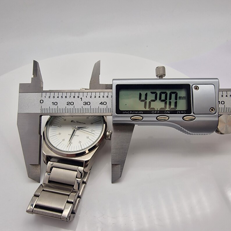 A authentic pre-owned Ben Sherman BS095 Men's Quartz Watch. Featuring a unique brushed silver analogue display, this timepiece stands out with its striking blue-accented numerical markers and precise 3-hand design. The durable stainless steel case is paired with a matching silver-toned metal link bracelet,