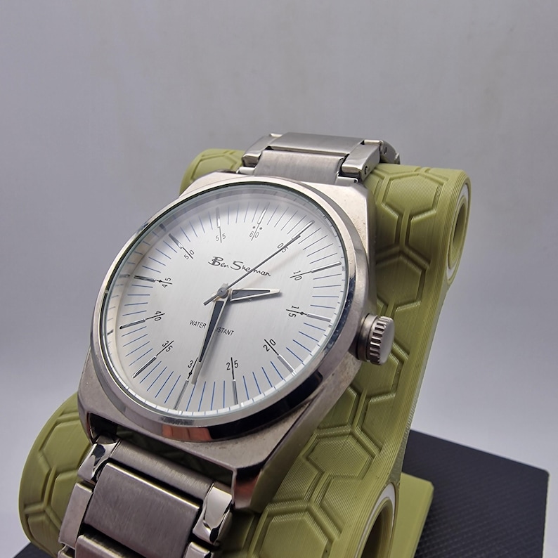 A authentic pre-owned Ben Sherman BS095 Men's Quartz Watch. Featuring a unique brushed silver analogue display, this timepiece stands out with its striking blue-accented numerical markers and precise 3-hand design. The durable stainless steel case is paired with a matching silver-toned metal link bracelet,