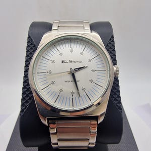 A authentic pre-owned Ben Sherman BS095 Men's Quartz Watch. Featuring a unique brushed silver analogue display, this timepiece stands out with its striking blue-accented numerical markers and precise 3-hand design. The durable stainless steel case is paired with a matching silver-toned metal link bracelet,