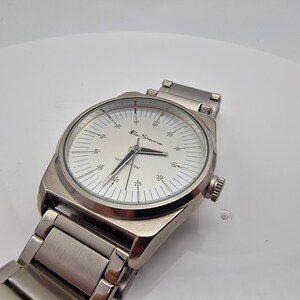 A authentic pre-owned Ben Sherman BS095 Men's Quartz Watch. Featuring a unique brushed silver analogue display, this timepiece stands out with its striking blue-accented numerical markers and precise 3-hand design. The durable stainless steel case is paired with a matching silver-toned metal link bracelet,