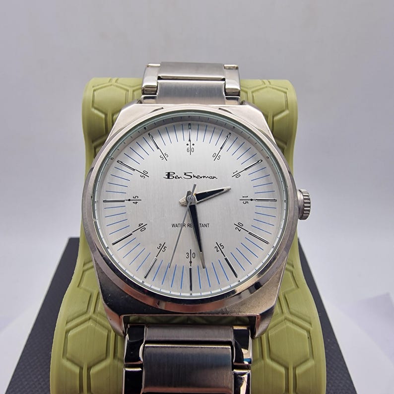 A authentic pre-owned Ben Sherman BS095 Men's Quartz Watch. Featuring a unique brushed silver analogue display, this timepiece stands out with its striking blue-accented numerical markers and precise 3-hand design. The durable stainless steel case is paired with a matching silver-toned metal link bracelet,
