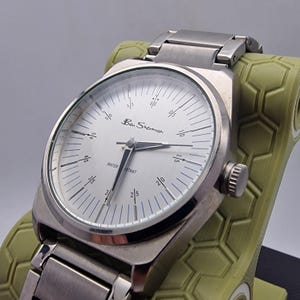 A authentic pre-owned Ben Sherman BS095 Men's Quartz Watch. Featuring a unique brushed silver analogue display, this timepiece stands out with its striking blue-accented numerical markers and precise 3-hand design. The durable stainless steel case is paired with a matching silver-toned metal link bracelet,