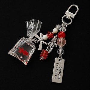 Sleutelhanger met goudvis in een tas — Y2K-visbedeltje, motiverend tasaccessoire met de tekst "Ik kies voor kracht".