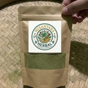 Puede incluir: Una bolsa de pie de papel kraft marrón con una ventana transparente que contiene polvo verde. La etiqueta presenta un logotipo circular con el texto NUSANTARA HERBAL TOKO ONLINE TERPERCAYA e ilustraciones de jengibre, canela y hojas verdes.