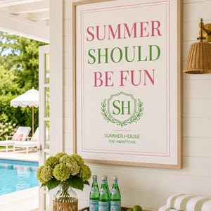 May include: A framed wall art print with a white background and a thin pink border. The text reads SUMMER SHOULD BE FUN in pink and green, with a green crest featuring the letters SH, and the text SUMMER HOUSE THE HAMPTONS in green below.