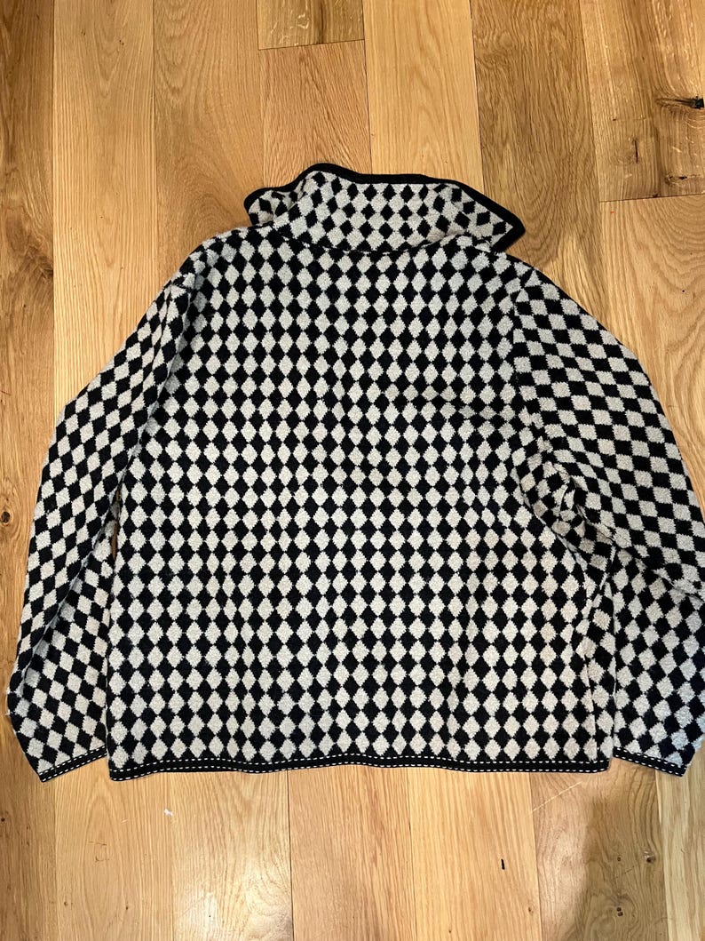 K&ouml;nnte beinhalten: Ein lang&auml;rmeliger Pullover mit einem sich wiederholenden schwarz-wei&szlig;en Rautenmuster auf dem gesamten Kleidungsst&uuml;ck. Der Pullover verf&uuml;gt &uuml;ber einen Umlegekragen sowie schwarze S&auml;ume an Kragen, &Auml;rmelb&uuml;ndchen und am unteren Saum.