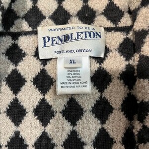 K&ouml;nnte beinhalten: Ein Kleidungsst&uuml;ck der Marke Pendleton mit einem schwarzen und beigen Rautenmuster. Das Innenetikett zeigt den Text: WARRANTED TO BE A PENDLETON, PORTLAND, OREGON, XL, RN#29685, 67% WOOL, 19% ACRYLIC, 14% NYLON, MADE IN HONG KONG.
