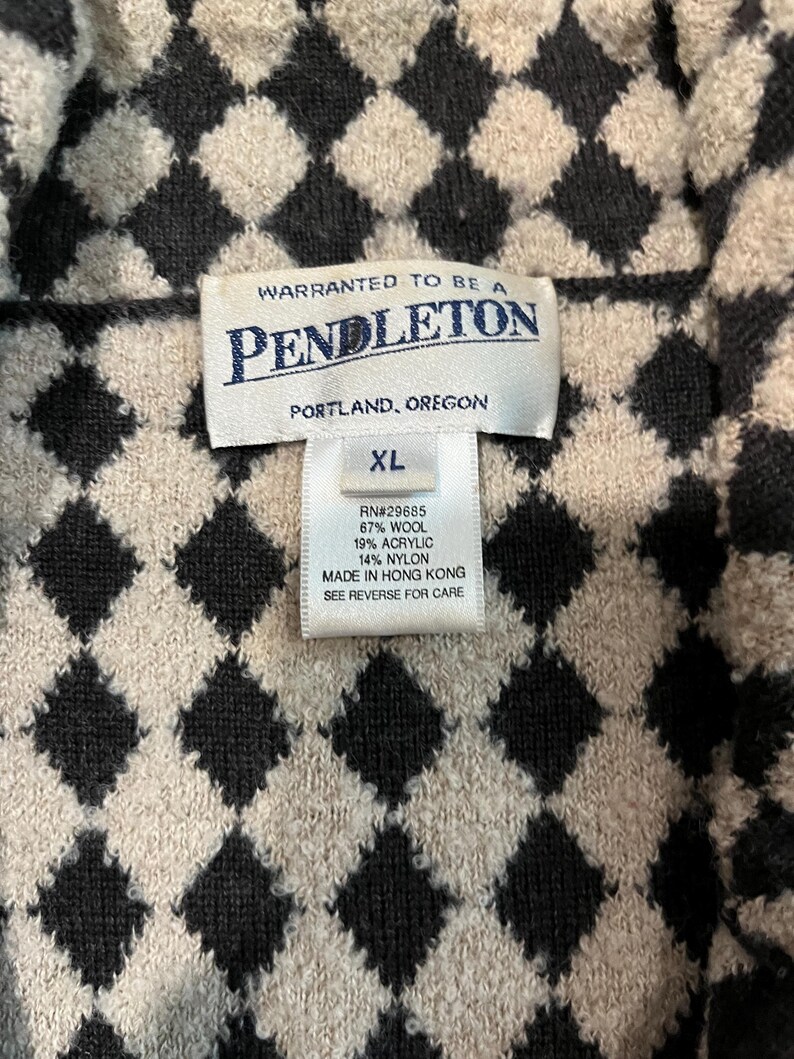 K&ouml;nnte beinhalten: Ein Kleidungsst&uuml;ck der Marke Pendleton mit einem schwarzen und beigen Rautenmuster. Das Innenetikett zeigt den Text: WARRANTED TO BE A PENDLETON, PORTLAND, OREGON, XL, RN#29685, 67% WOOL, 19% ACRYLIC, 14% NYLON, MADE IN HONG KONG.