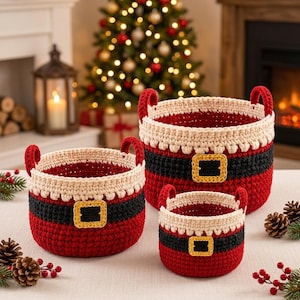 May include: A set of three round crochet baskets in varying sizes, designed to resemble Santa Claus suits. Each basket features a red base, a black band, a cream-coloured top rim, and a central gold-coloured buckle detail with two small handles.