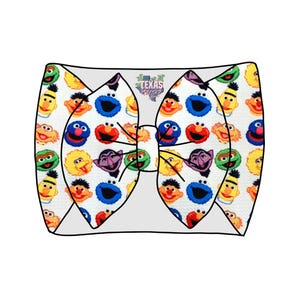 Peut inclure: Un nœud pour cheveux en tissu blanc avec un motif répétitif de visages de personnages de Sesame Street, dont Elmo, Cookie Monster, Big Bird, Bert, Ernie et le Comte von Count. Le centre du nœud affiche le texte Texas Gypsy Bows.
